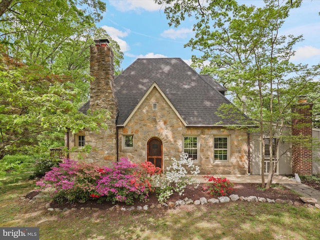 tudor home featuring stone siding, a chimney, and roof with shingles