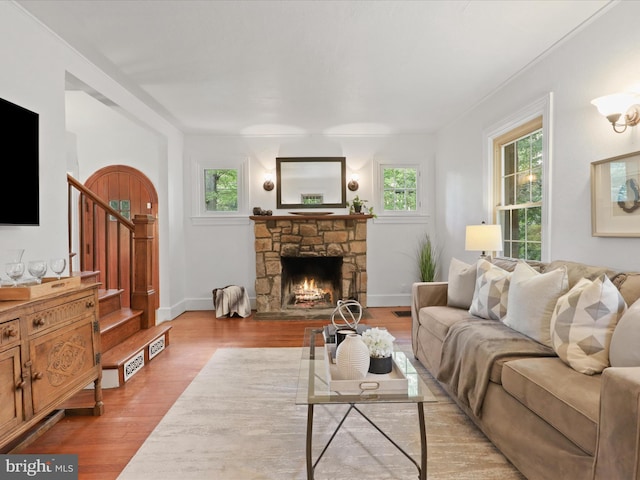 living area with stairway, wood finished floors, a stone fireplace, and baseboards
