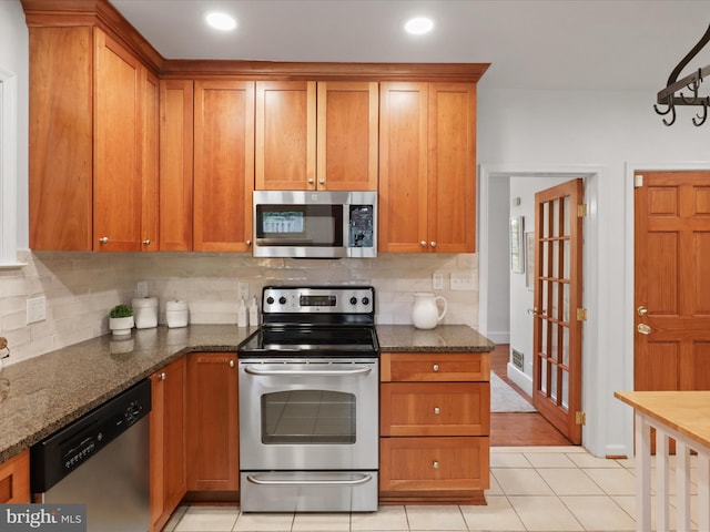 kitchen with appliances with stainless steel finishes, decorative backsplash, brown cabinetry, dark stone countertops, and recessed lighting
