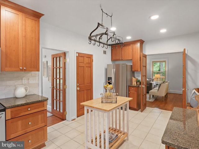 kitchen with dark stone counters, recessed lighting, light tile patterned flooring, a chandelier, and stainless steel refrigerator with ice dispenser