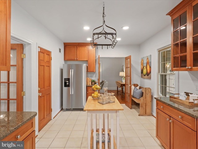 kitchen featuring stainless steel fridge, glass insert cabinets, dark stone counters, recessed lighting, and pendant lighting