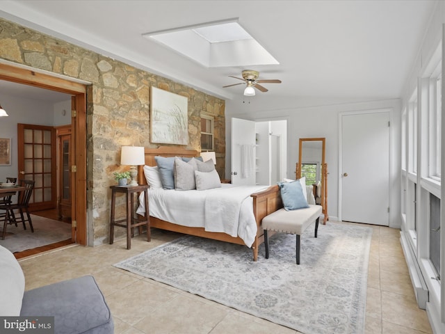 bedroom featuring light tile patterned floors, a skylight, ceiling fan, and ensuite bathroom