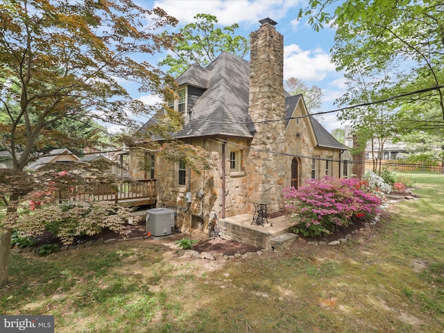 rear view of house featuring stone siding, a wooden deck, and a chimney