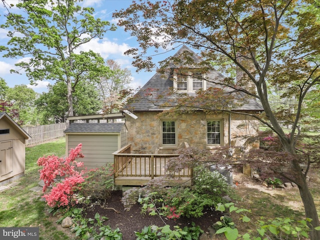 back of house featuring a shed, fence, an outbuilding, stone siding, and a wooden deck