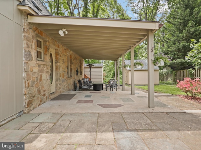 view of patio / terrace featuring a storage unit, an outbuilding, a carport, fence, and a fire pit
