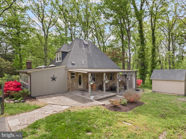 back of property with stone siding, a lawn, an outbuilding, a chimney, and a shingled roof