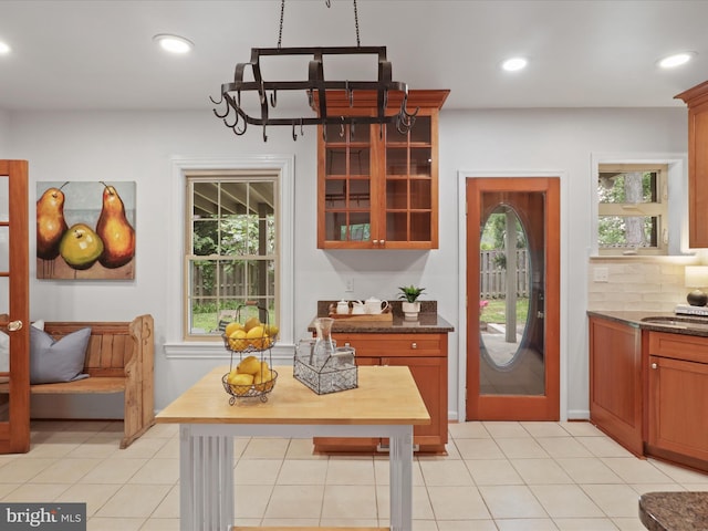 kitchen featuring recessed lighting, glass insert cabinets, a chandelier, decorative backsplash, and dark stone counters