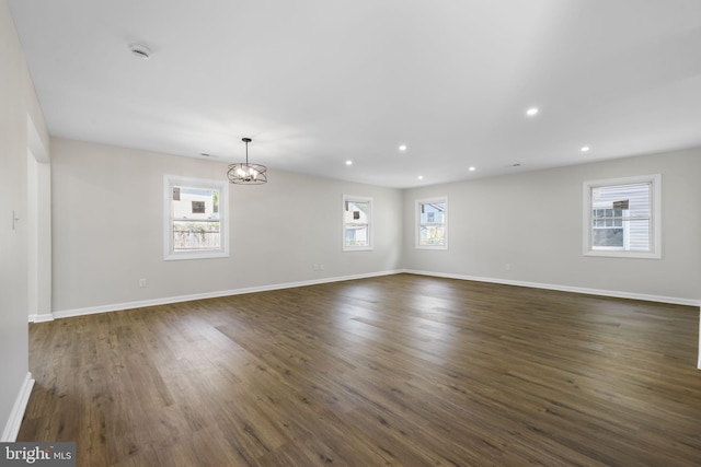 unfurnished room with recessed lighting, baseboards, dark wood finished floors, and an inviting chandelier