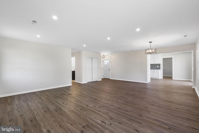 unfurnished living room featuring baseboards, recessed lighting, a notable chandelier, and dark wood-style floors