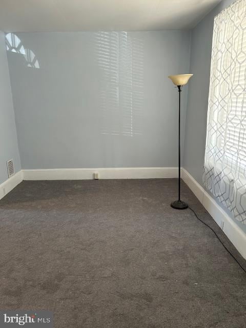 spare room with baseboards, dark carpet, and visible vents