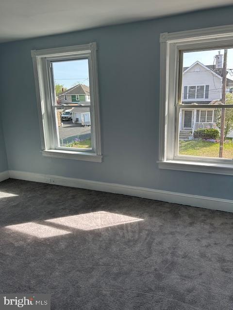 spare room featuring baseboards and dark colored carpet