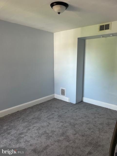 empty room with baseboards, visible vents, and dark colored carpet