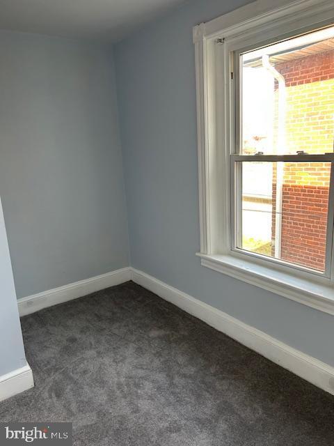 empty room with a healthy amount of sunlight, baseboards, and dark colored carpet