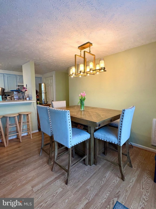 dining room with light wood-style floors, a textured ceiling, baseboards, and an inviting chandelier