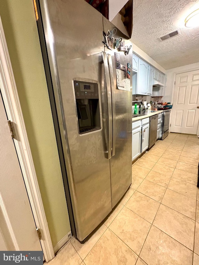 kitchen with light countertops, a textured ceiling, stainless steel appliances, light tile patterned floors, and visible vents