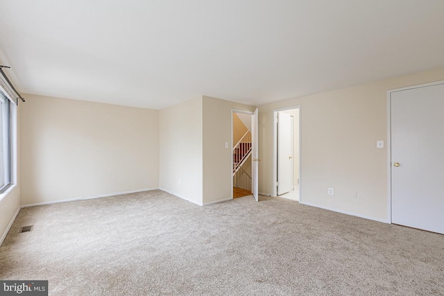 empty room featuring light carpet, stairs, baseboards, and visible vents