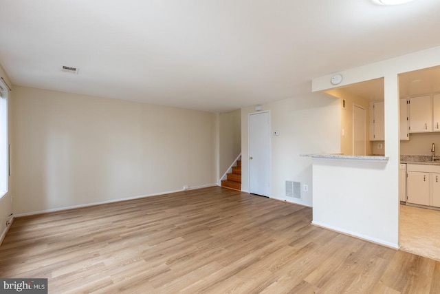unfurnished living room featuring light wood finished floors, a sink, visible vents, baseboards, and stairway