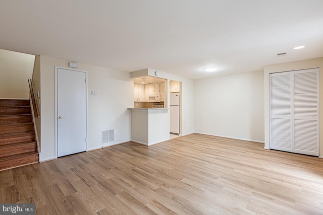 unfurnished living room featuring baseboards, light wood-style floors, visible vents, and stairway