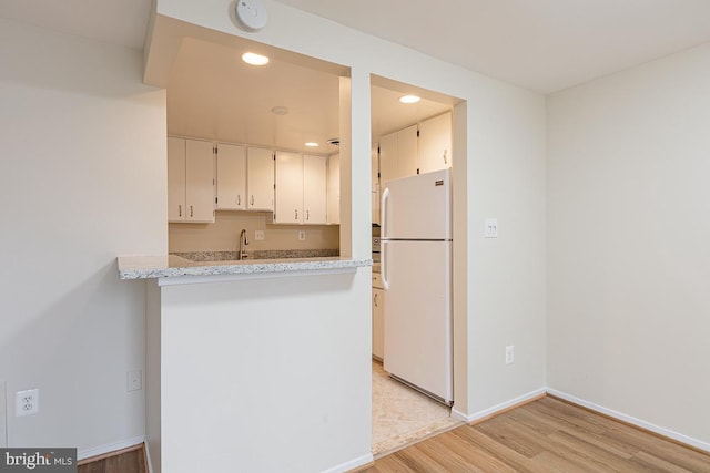 kitchen featuring a peninsula, freestanding refrigerator, baseboards, light wood-style floors, and recessed lighting
