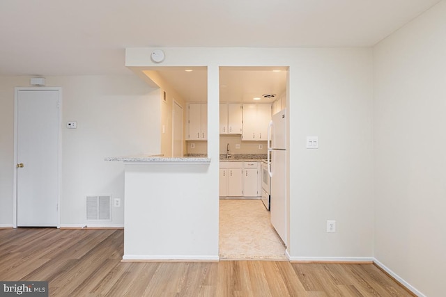 kitchen with a sink, freestanding refrigerator, visible vents, light countertops, and light wood-style floors