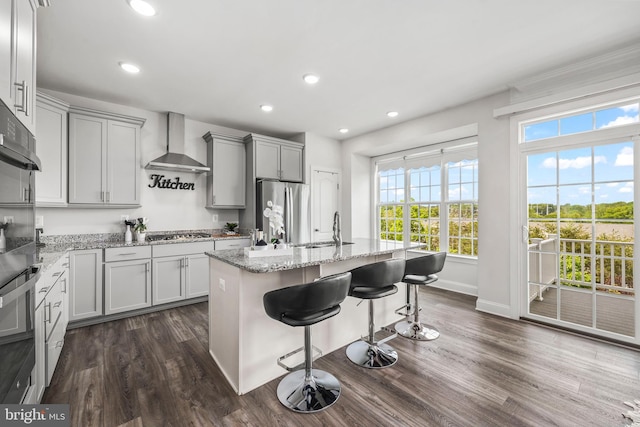 kitchen with wall chimney range hood, appliances with stainless steel finishes, a sink, baseboards, and dark wood-type flooring