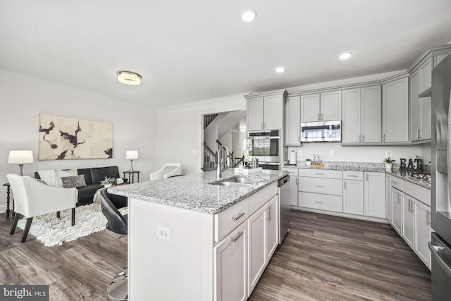kitchen with appliances with stainless steel finishes, a center island with sink, a sink, light stone counters, and ornamental molding