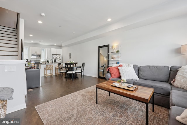 living area with dark wood-type flooring, recessed lighting, stairs, and baseboards
