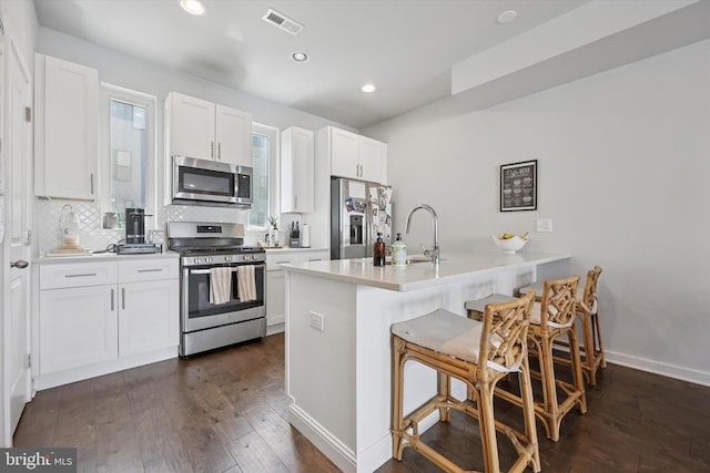 kitchen featuring visible vents, appliances with stainless steel finishes, a sink, a peninsula, and dark wood-type flooring