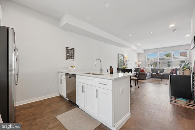kitchen featuring white cabinets, a sink, stainless steel appliances, a peninsula, and dark wood-type flooring