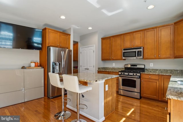 kitchen with light stone countertops, stainless steel appliances, brown cabinets, and wood finished floors