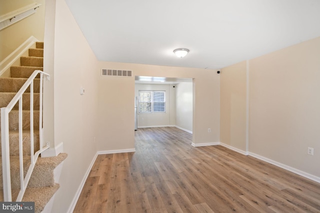 empty room with visible vents, baseboards, wood finished floors, and stairway