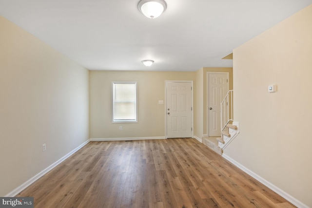 empty room with baseboards, stairs, and wood finished floors
