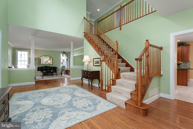 stairway featuring decorative columns, ornamental molding, wood finished floors, baseboards, and a high ceiling