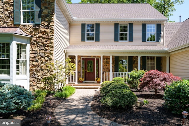 view of exterior entry with stone siding, a porch, and roof with shingles