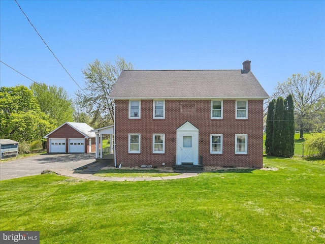 colonial inspired home featuring a detached garage, brick siding, a chimney, and a front yard
