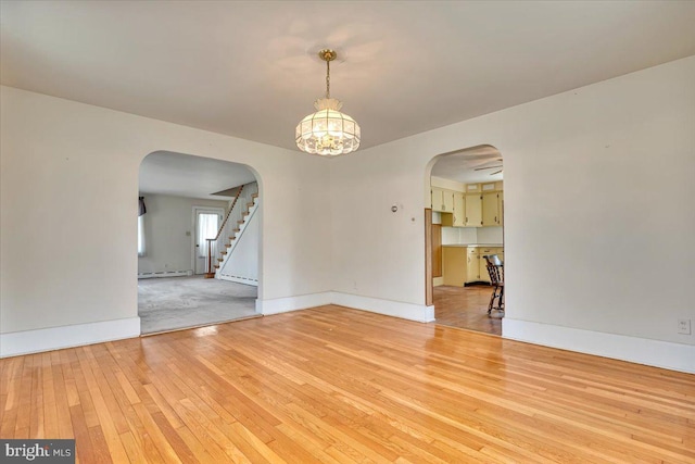 unfurnished room featuring arched walkways, stairway, baseboards, light wood finished floors, and an inviting chandelier