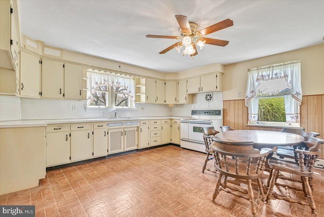 kitchen with white range with electric stovetop, wainscoting, ceiling fan, and cream cabinetry
