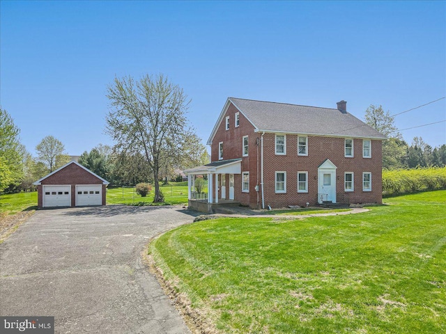 colonial inspired home featuring a front lawn, brick siding, a detached garage, a chimney, and an outdoor structure