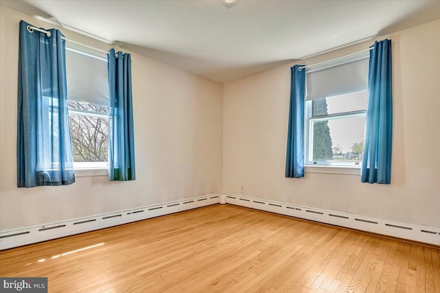 unfurnished room with plenty of natural light, baseboard heating, and hardwood / wood-style flooring