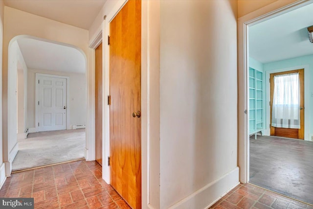 corridor featuring arched walkways, brick floor, and baseboards