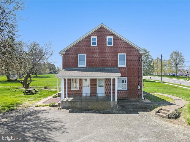 view of front of house featuring covered porch, a front yard, and brick siding