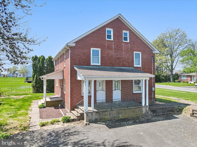 view of front facade featuring brick siding, covered porch, and a front yard