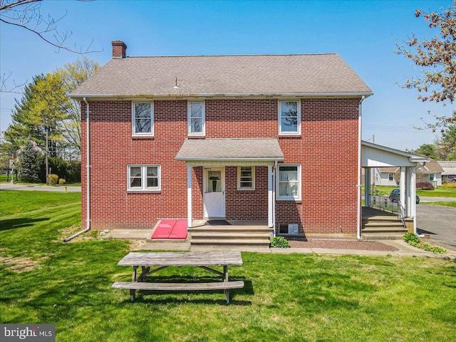 back of property with a chimney, brick siding, a shingled roof, a yard, and a carport