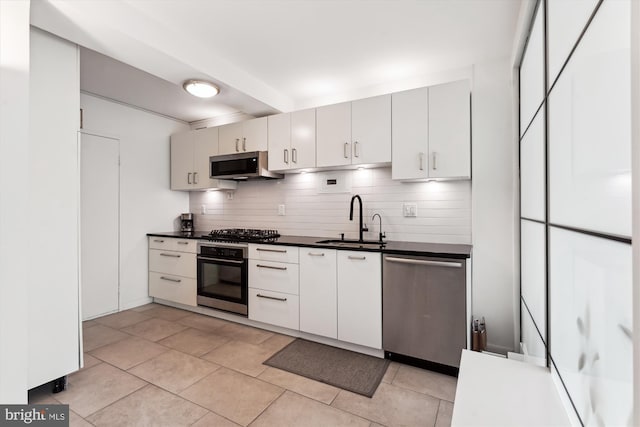 kitchen featuring light tile patterned flooring, dark countertops, a sink, stainless steel appliances, and decorative backsplash