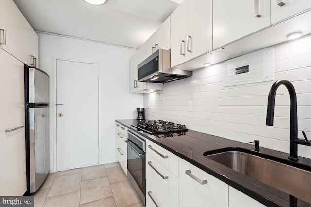 kitchen featuring dark countertops, a sink, light tile patterned floors, white cabinets, and black appliances