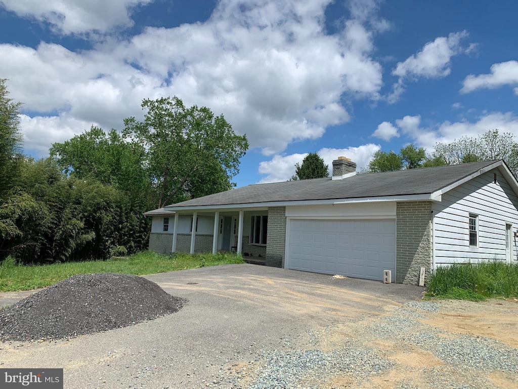 single story home featuring asphalt driveway, a garage, a chimney, and brick siding