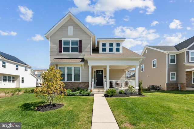 view of front of property with a shingled roof, covered porch, stone siding, and a front yard