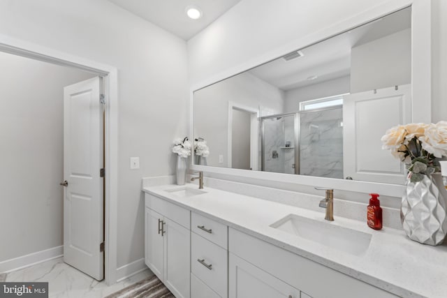 full bathroom featuring double vanity, a sink, a marble finish shower, and baseboards