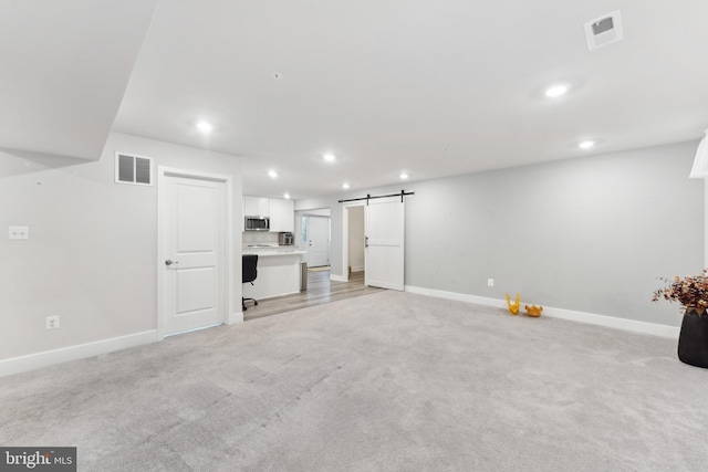 unfurnished living room featuring visible vents, a barn door, and baseboards