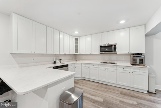 kitchen with white cabinets, a peninsula, stainless steel microwave, and light wood finished floors